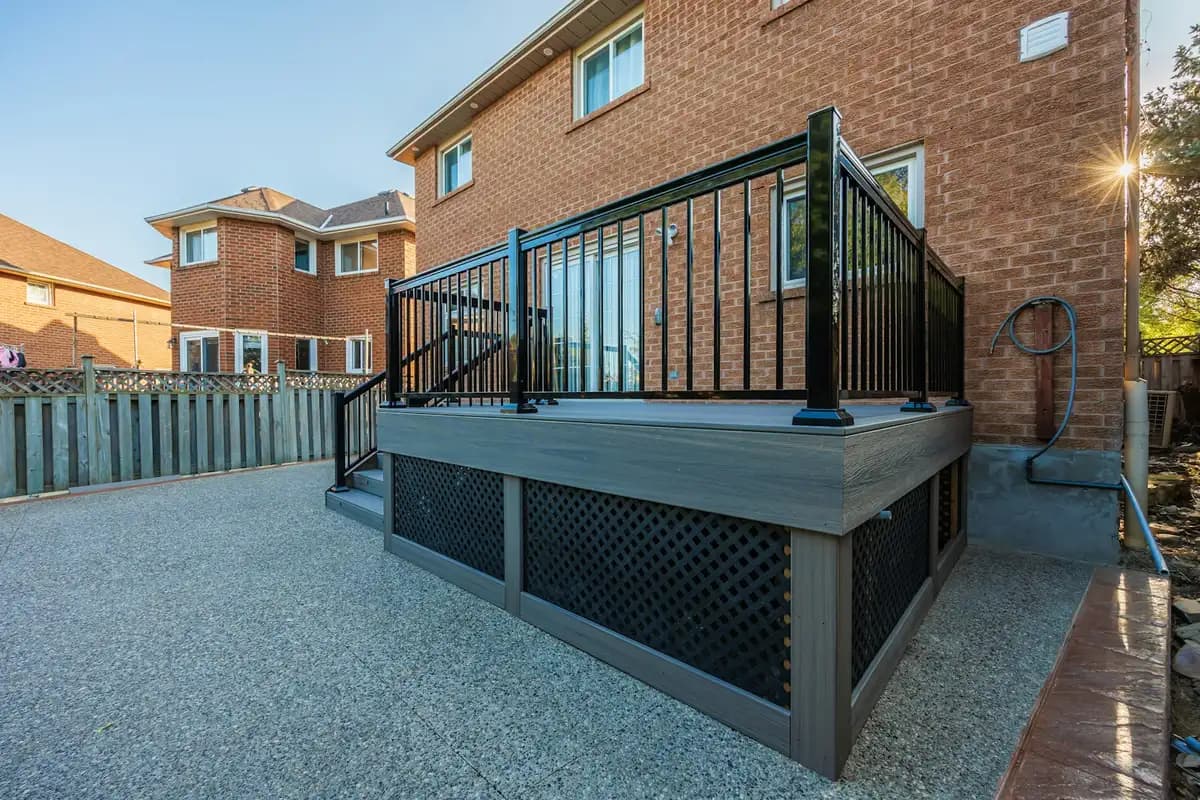 Gray woodgrain composite deck with black aluminum baluster railing and lattice skirting beside a brick two-story house
