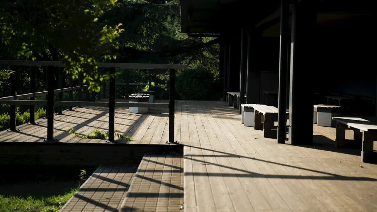 Wide low wooden deck with built-in benches and a single step, in dappled afternoon light