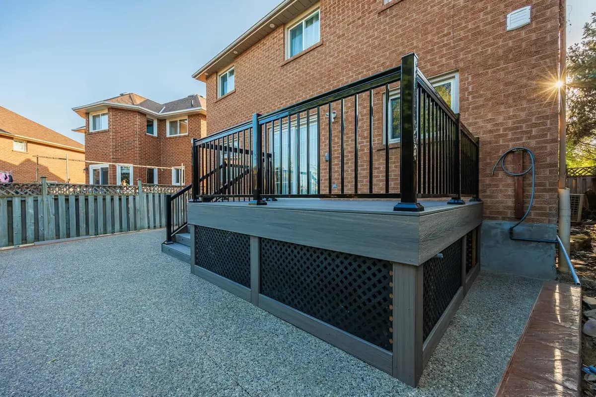 Raised composite deck with black aluminum railing and lattice skirting behind a brick house