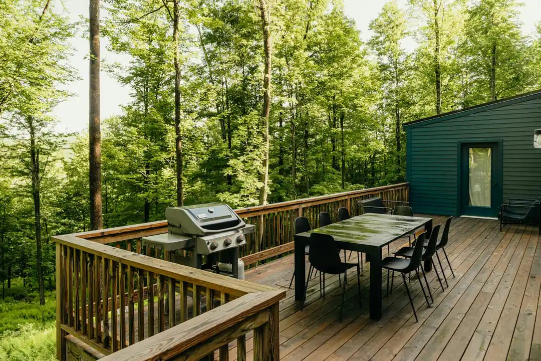 Elevated wood deck with a gas grill and an eight-seat dining table overlooking woods