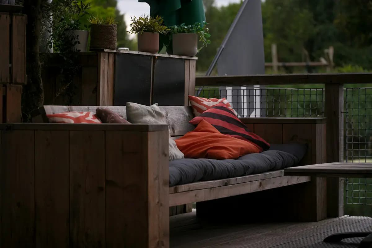 Built-in wooden bench sofa with cushions in the corner of a small wood deck