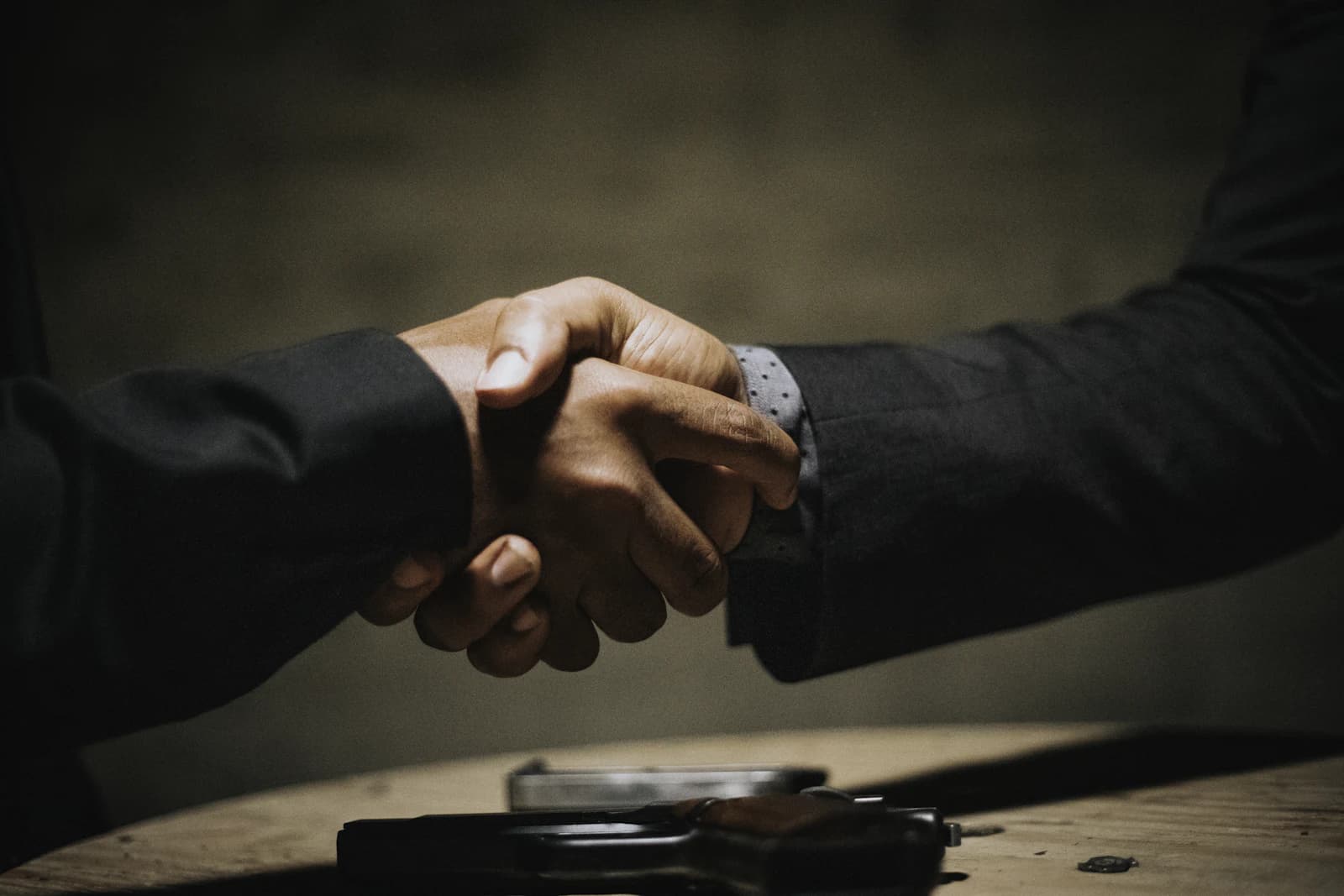 Two people shaking hands over a wooden table after reaching an agreement