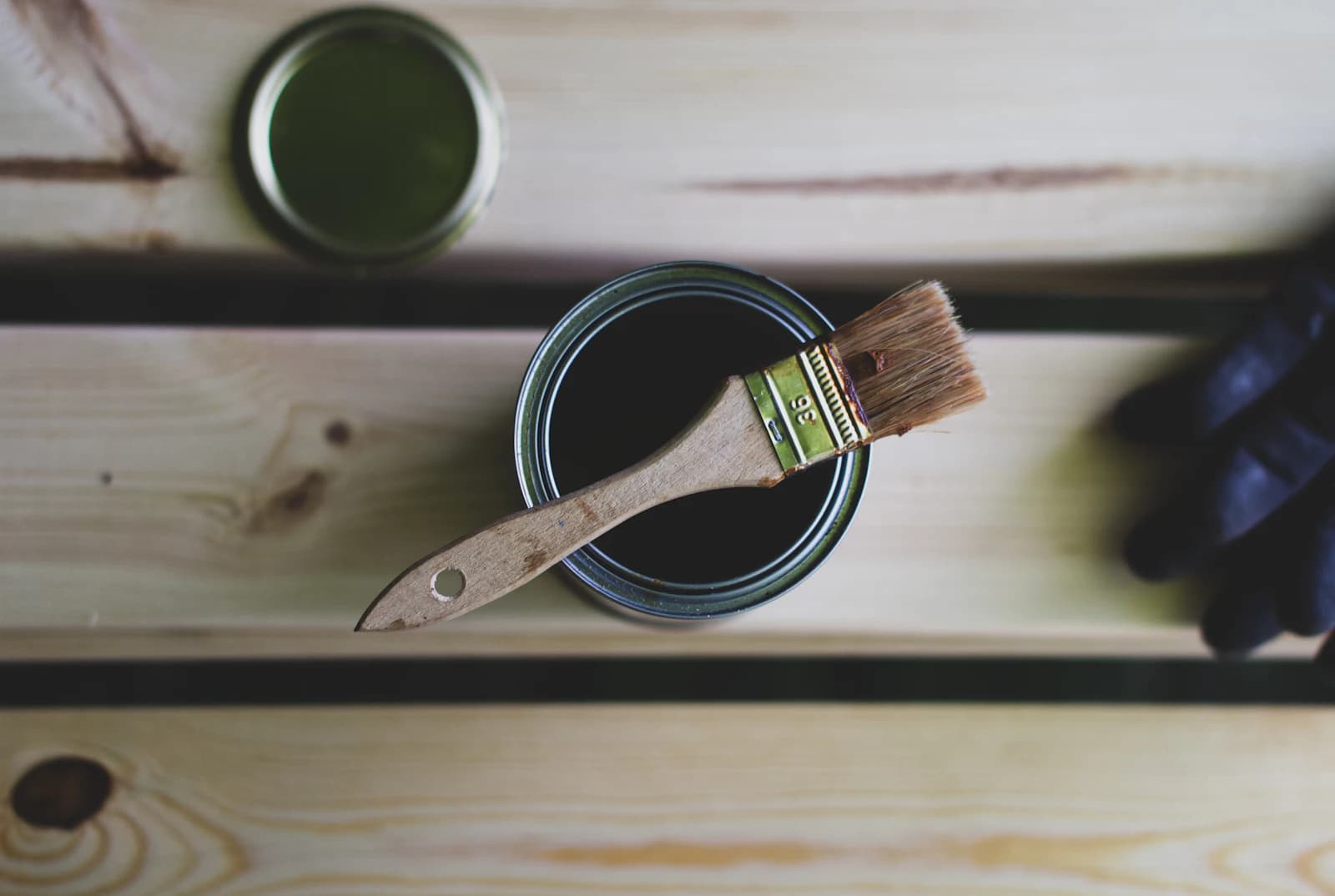 A brush applying wood stain along the boards of a deck, leaving a rich tone
