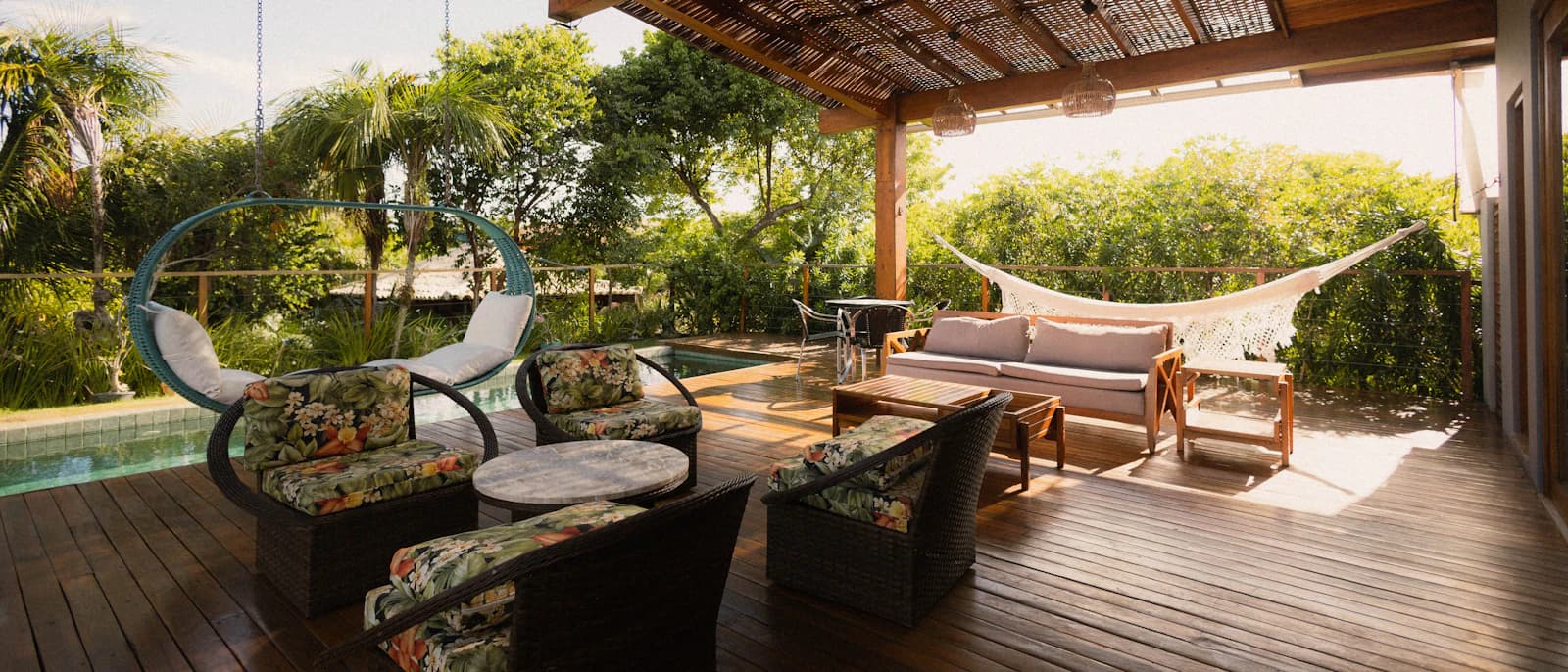 A covered outdoor deck with seating and a hammock overlooking a swimming pool