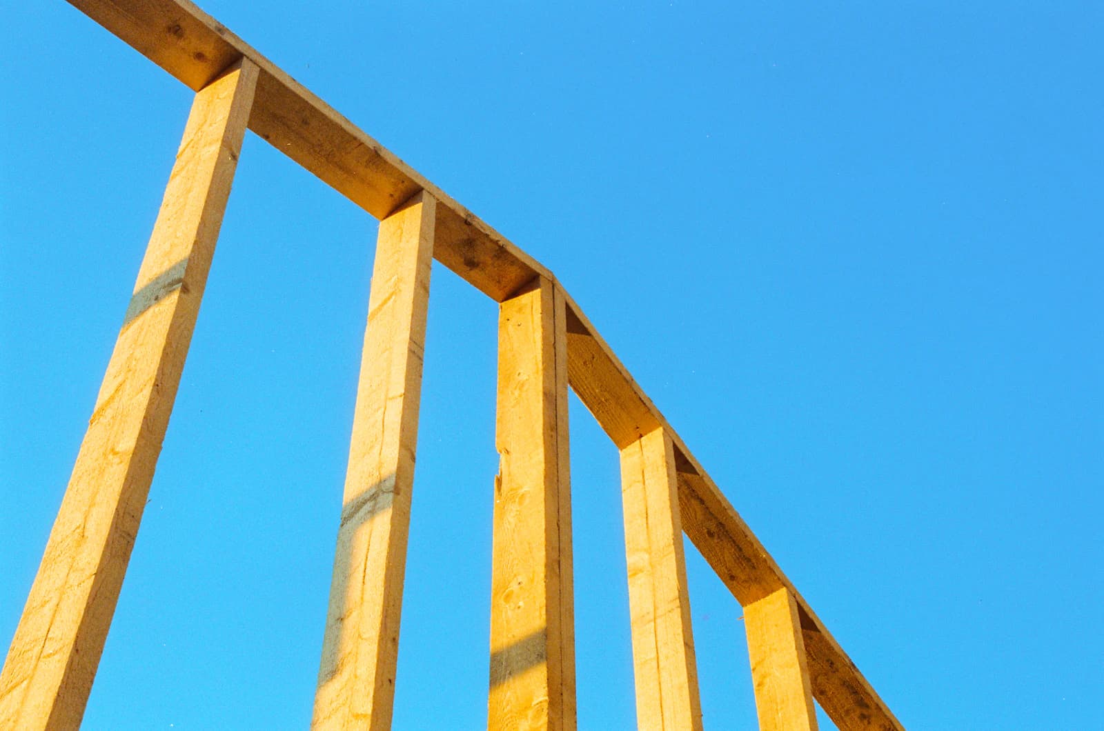 A pressure-treated wooden deck frame of joists and beams under a clear blue sky